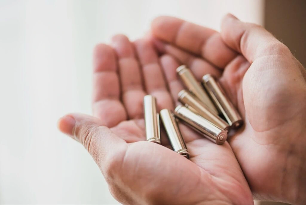 Cupped hands holding a collection of silver cylindrical batteries.