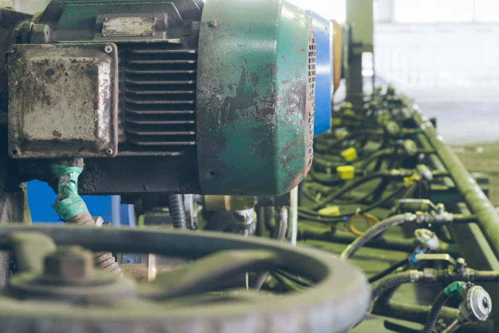 Weathered green electric motor and row of industrial valves inside a steel factory.