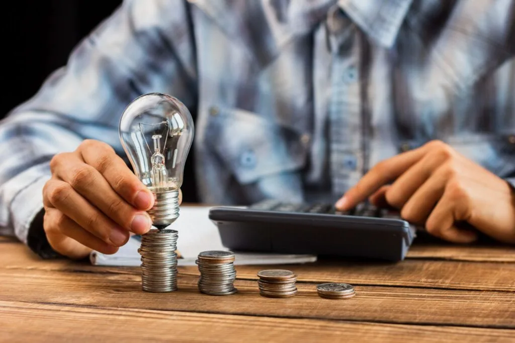 Person calculating energy costs with a light bulb on a stack of coins.